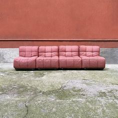 a pink couch sitting in front of a red wall on the ground next to a concrete slab