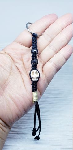 a hand holding a black and white beaded key chain with a skull on it