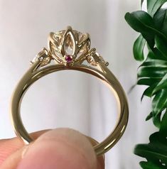 a person holding up a gold ring with two diamonds on it and a pink diamond in the center