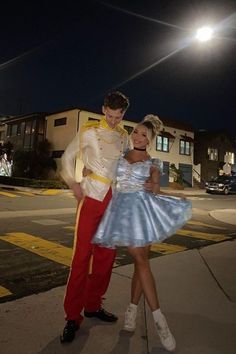 a man and woman dressed in costumes standing next to each other on the sidewalk at night