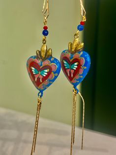 Heart shaped pendant earrings handmade by Edith Orozco, from Leon, Guanajuato, Mexico! Edith paints each heart amulet by hand, then carefully sets them in gold plated fixtures. Every piece is unique. Heart Amulet, Mexican Gifts, Heart Shaped Pendant, Happy Hippie, Pendant Earring, Heart Shape Pendant, Scarf Jewelry, Handmade Clothes, Pendant Earrings