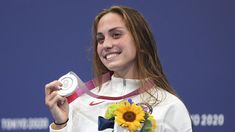 a woman holding up a medal in front of a blue wall with flowers on it