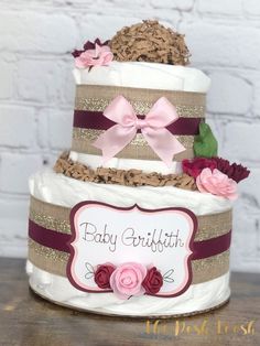 a three tiered cake with pink flowers on top and brown ribbon around the bottom