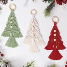 three crocheted christmas tree ornaments hanging from wooden hooks on a white surface surrounded by pine branches