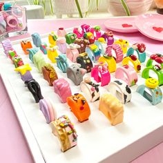 there are many small toy animals on the white trays and pink plates behind them