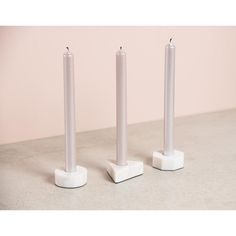 three white candles sitting on top of each other in front of a light pink wall