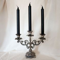 three black candles sitting on top of a metal candelabra