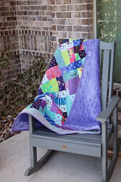 a rocking chair with a quilt on it and a purple blanket draped over the seat