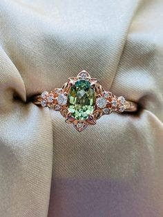 an engagement ring with green and white stones on it's side, sitting on top of a beige cloth