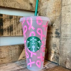 a starbucks cup with pink and green designs on the side sitting on a wooden table