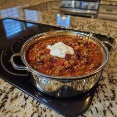 a large pot filled with chili and sour cream on top of a stove burner