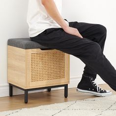 a man sitting on top of a wooden bench next to a white rug and wall