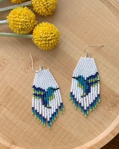 a pair of earrings sitting on top of a wooden table next to yellow dandelions