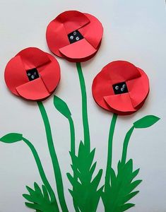 three red paper flowers with green stems on a white background, cut out to look like they are growing from the ground