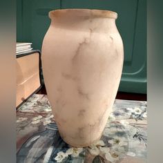 a white vase sitting on top of a table next to a green wall and carpet