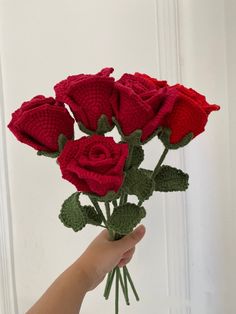 a hand holding a crocheted red rose bouquet in front of a white door