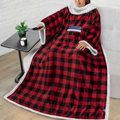 a woman sitting on a couch wearing a red and black plaid blanket with white trim