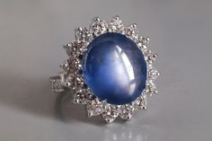 a ring with a large blue stone surrounded by small white diamonds on a gray surface