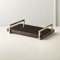 a black marble tray with gold handles on a white countertop in front of a white wall