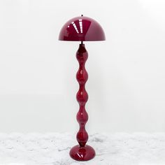 a red table lamp sitting on top of a white floor next to a light bulb