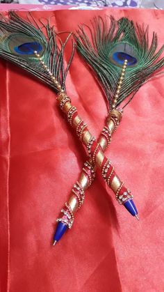 two peacock feathers are attached to some beads on a piece of red material with gold trim