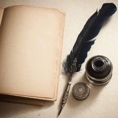 an old book, quill pen and inkwell sitting on a table next to it