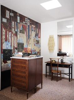 a room with a painting on the wall next to a desk and chair in it