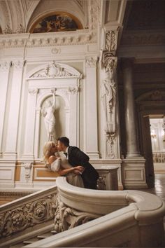 a bride and groom are kissing on the stairs at their wedding reception in an ornate building