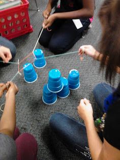 several people are sitting on the floor playing with cups and threading them to strings