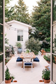 an outdoor dining area is seen through the open door to a backyard with potted plants