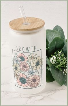 a white jar with flowers on it and a bamboo lid next to some green leaves