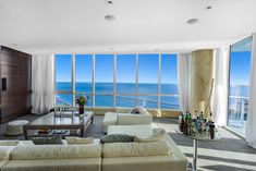 a living room filled with furniture and large windows overlooking the ocean on a sunny day