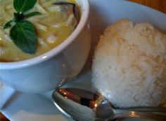 a white plate topped with rice and a bowl filled with soup next to a spoon