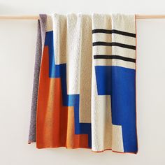 a blanket hanging on a clothes line next to a white wall with an orange, blue and black stripe