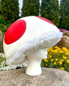 a white and red mushroom hat sitting on top of a rock in front of flowers