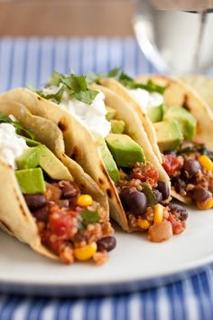 three tacos on a white plate with avocado, black beans and sour cream