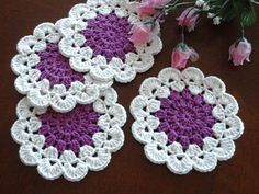 three crocheted coasters sitting on top of a table next to pink flowers