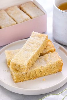 two pieces of cake on a plate next to a cup of tea and a pink box