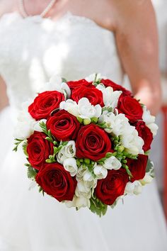 a bride holding a bouquet of red and white flowers