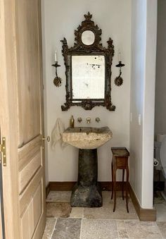 a bathroom with a pedestal sink and mirror on the wall, next to a wooden door