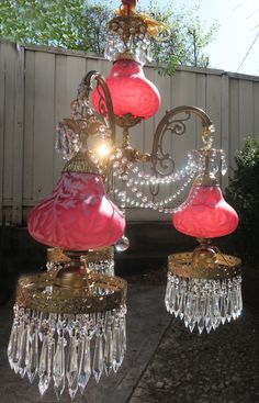 two pink and gold chandeliers hanging from a ceiling in front of a white fence