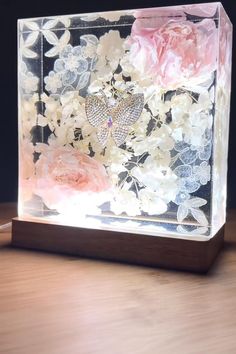 a glass block with flowers and butterflies in it on top of a wooden table next to a phone charger