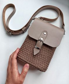 a hand holding a brown and beige bag on top of a white table with a strap