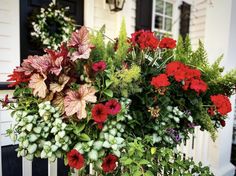 red and green flowers are growing on the side of a white porch railing in front of a house