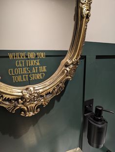 there is a gold mirror hanging on the wall in this bathroom that says where did you get those clothes at the toilet store?