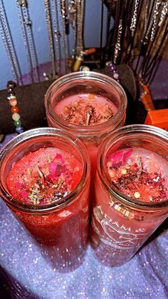 three jars filled with pink liquid sitting on top of a purple table cloth next to other items