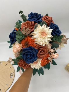 a bridal bouquet with blue, orange and white flowers on it next to a clock