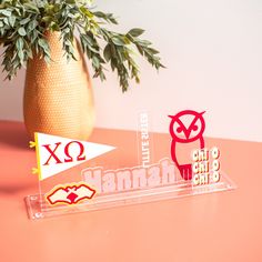 two acrylic signs sitting on top of a table next to a potted plant