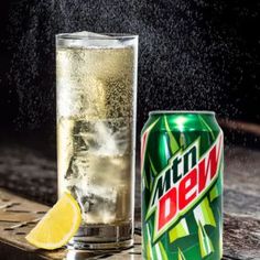 a can of mountain dew next to a glass filled with water and lemon wedges