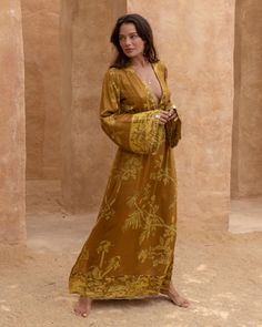 a woman standing in front of some pillars wearing a long dress with an intricate design